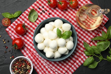 Photo of Tasty mozzarella cheese balls in bowl, tomatoes and spices on black table, flat lay