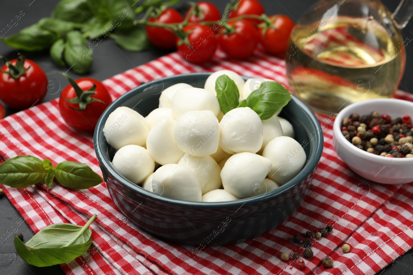 Tasty mozzarella cheese balls in bowl, tomatoes and spices on black table, closeup Photo of Tasty mozzarella cheese balls in bowl, tomatoes and spices on black table, closeup