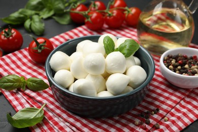 Photo of Tasty mozzarella cheese balls in bowl, tomatoes and spices on black table, closeup