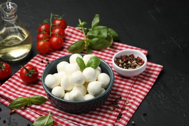 Photo of Tasty mozzarella cheese balls in bowl, tomatoes and spices on black table, closeup