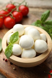 Photo of Tasty mozzarella cheese balls in bowl, basil, peppercorns and tomatoes on table, closeup