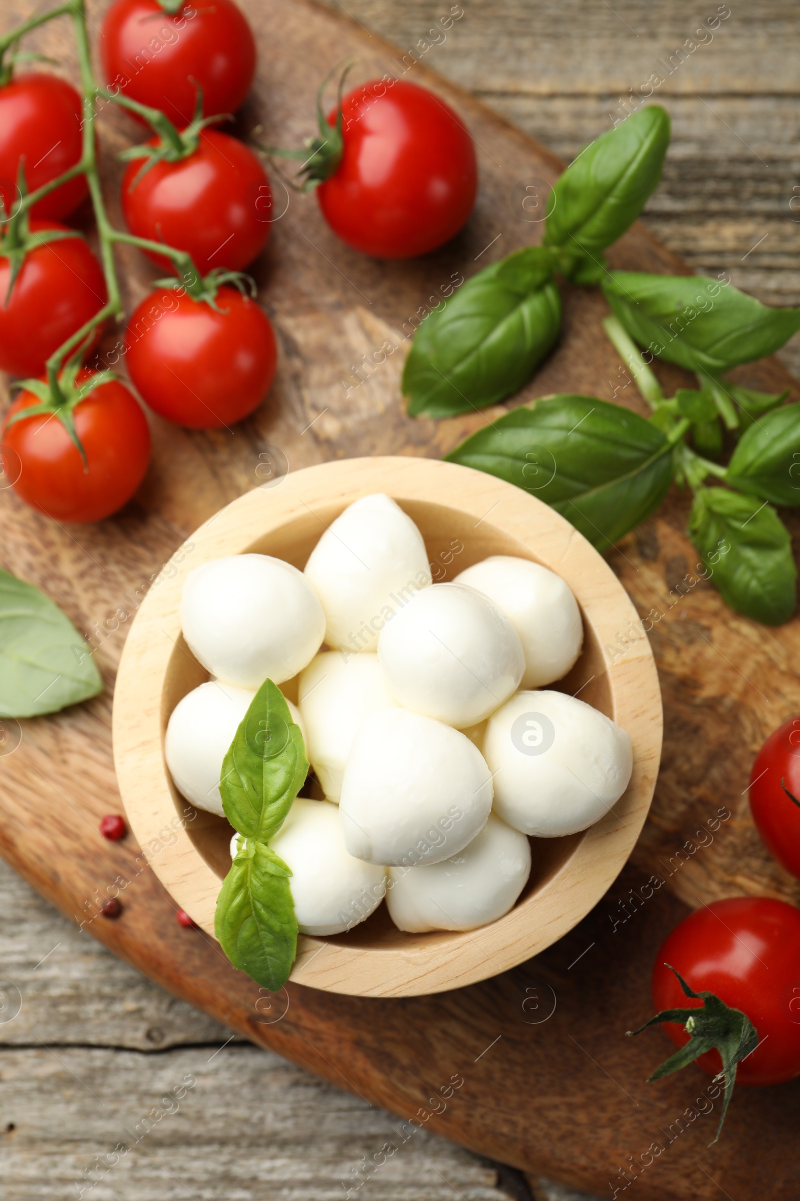Tasty mozzarella cheese balls in bowl, basil, peppercorns and tomatoes on wooden table, top view Photo of Tasty mozzarella cheese balls in bowl, basil, peppercorns and tomatoes on wooden table, top view