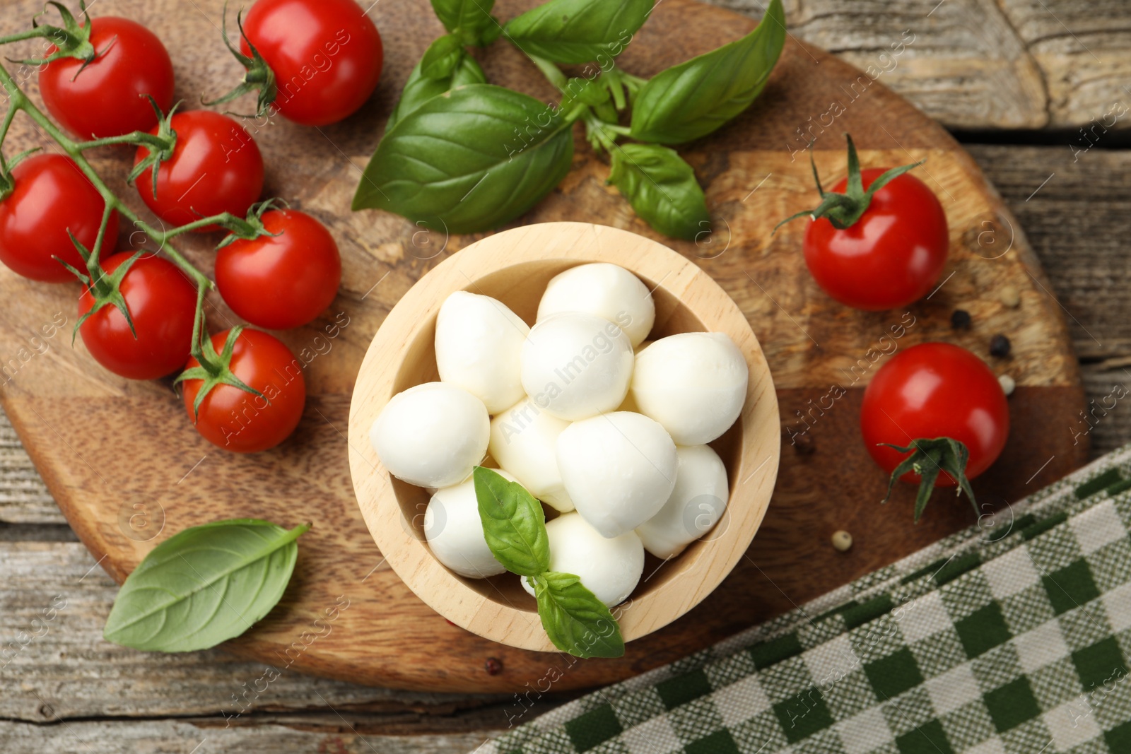Tasty mozzarella cheese balls in bowl, basil, peppercorns and tomatoes on wooden table, top view Photo of Tasty mozzarella cheese balls in bowl, basil, peppercorns and tomatoes on wooden table, top view