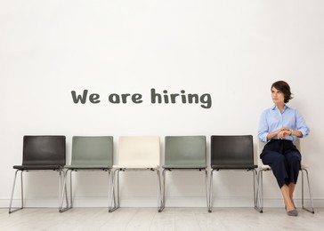 Image of We Are Hiring. Young woman sitting on chair and waiting for job interview near light wall. Recruitment, human resource concept