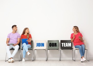 Image of Empty office chairs with words Join Our Team. Group of young people waiting for job interview near light wall. Recruitment, human resource concept