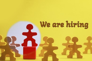 Image of We Are Hiring. Wooden figures with red one on top of cube on yellow background. Recruitment, human resource concept