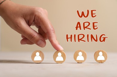 Image of We Are Hiring. Woman touching wooden circle with human icon among others on beige background, closeup. Recruitment, human resource concept