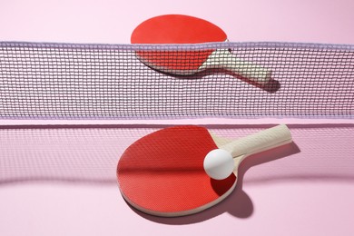 Photo of Ping pong rackets, ball and net on pink background, above view