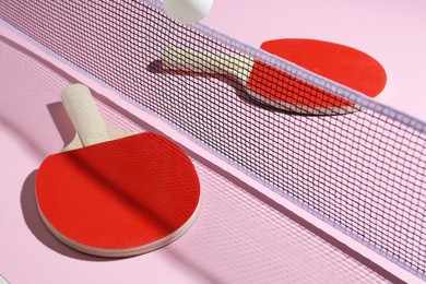 Photo of Ping pong rackets, ball and net on pink background, closeup