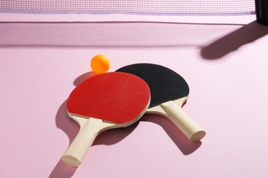 Photo of Ping pong rackets, ball and net on pink background, above view