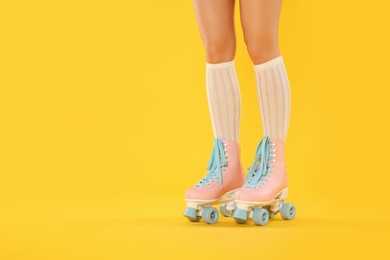 Photo of Woman in roller skates on orange background, closeup. Space for text