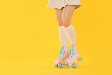 Photo of Woman in roller skates on orange background, closeup. Space for text
