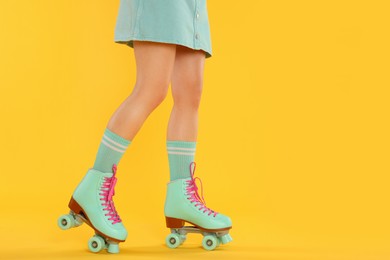 Photo of Woman in roller skates on orange background, closeup. Space for text