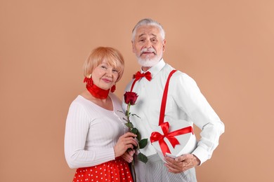 Photo of Lovely senior couple with gift box and rose on light brown background