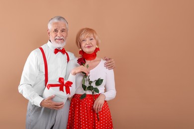 Photo of Lovely senior couple with gift box and rose on light brown background, space for text