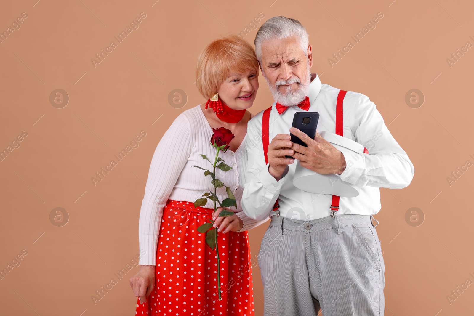 Lovely senior couple with rose and smartphone on light brown background Photo of Lovely senior couple with rose and smartphone on light brown background