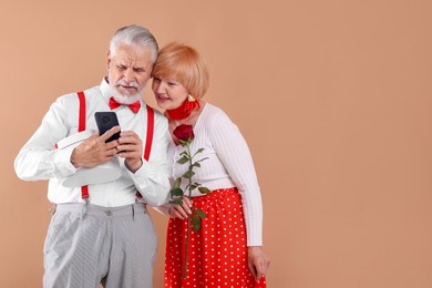 Photo of Lovely senior couple with rose and smartphone on light brown background, space for text