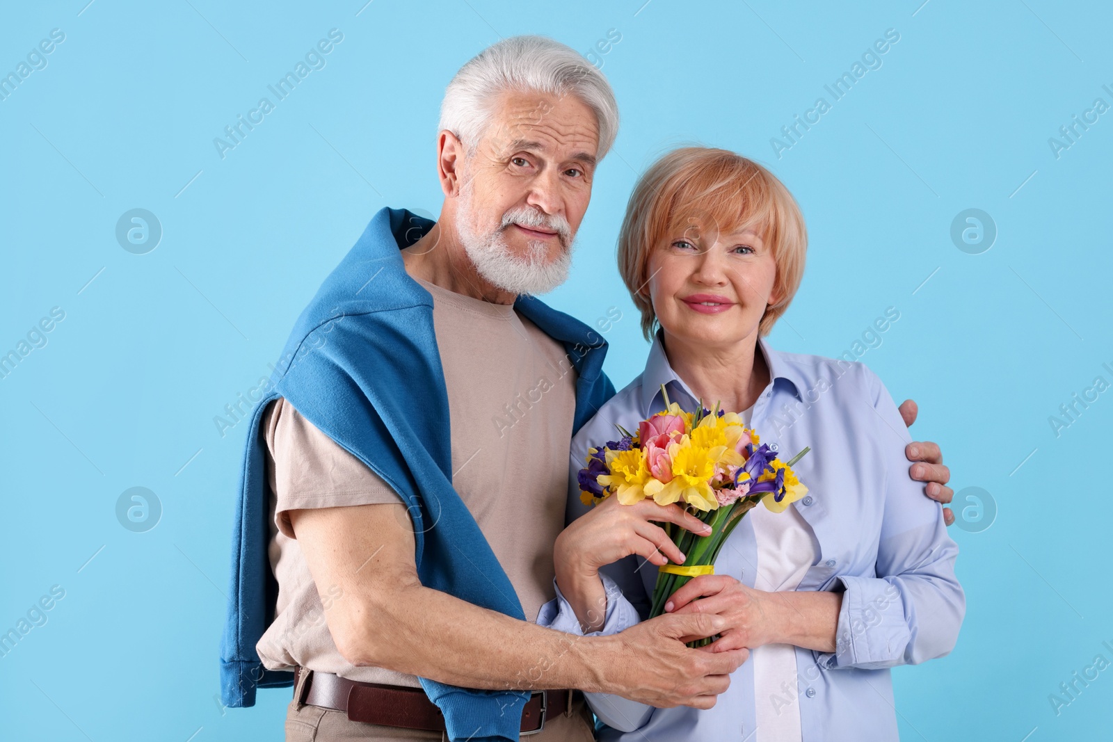 Lovely senior couple with bouquet of flowers on light blue background Photo of Lovely senior couple with bouquet of flowers on light blue background