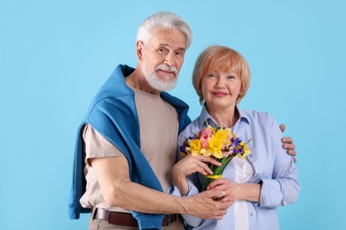 Photo of Lovely senior couple with bouquet of flowers on light blue background