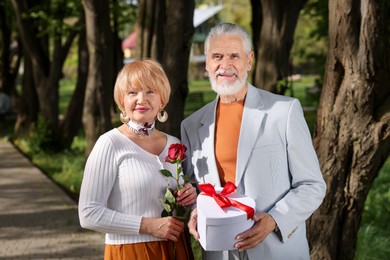 Photo of Lovely senior couple with gift box and rose in park