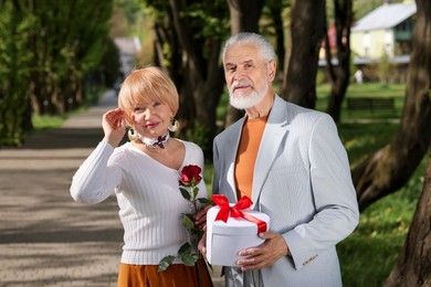 Photo of Lovely senior couple with gift box and rose in park