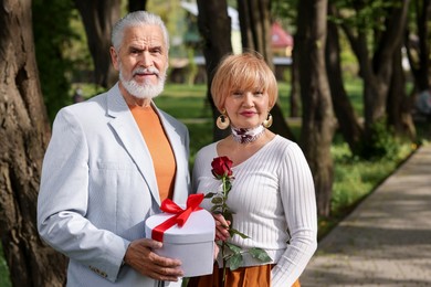 Photo of Lovely senior couple with gift box and rose in park