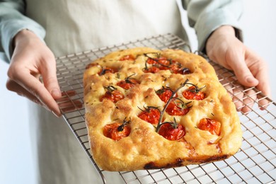 Photo of Woman holding delicious focaccia with tomatoes and spices on light background, closeup
