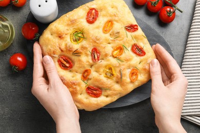 Photo of Woman with delicious focaccia with tomatoes and spices at gray textured table, top view