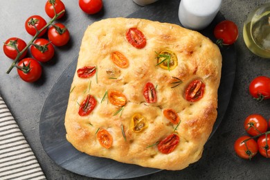 Photo of Delicious focaccia with tomatoes, spices and oil on gray table, flat lay