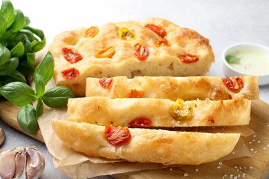 Photo of Cut delicious focaccia with tomatoes, spices and oil on gray table, closeup