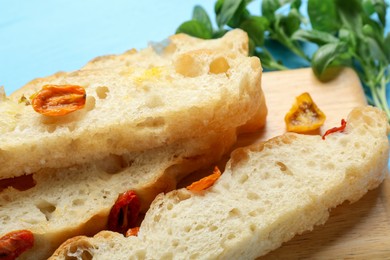 Photo of Pieces of delicious focaccia with tomatoes and basil on light blue table, closeup