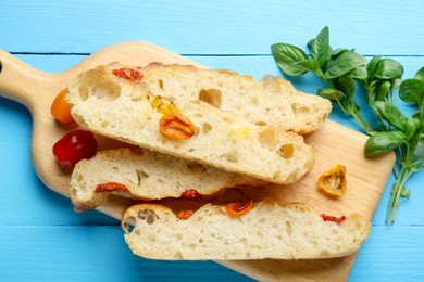 Photo of Pieces of delicious focaccia with tomatoes and basil on light blue wooden table, flat lay