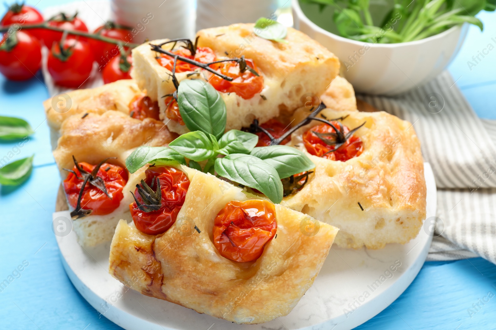Pieces of delicious focaccia with tomatoes and basil on light blue wooden table, closeup Photo of Pieces of delicious focaccia with tomatoes and basil on light blue wooden table, closeup