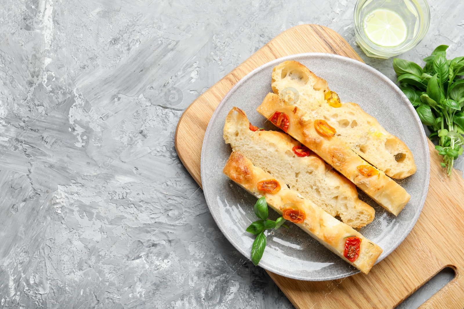 Pieces of delicious focaccia with tomatoes, basil and glass of water on gray textured table, flat lay. Space for text Photo of Pieces of delicious focaccia with tomatoes, basil and glass of water on gray textured table, flat lay. Space for text