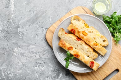 Photo of Pieces of delicious focaccia with tomatoes, basil and glass of water on gray textured table, flat lay. Space for text