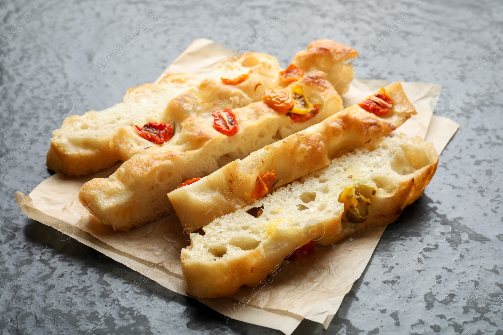 Pieces of delicious focaccia with tomatoes on gray textured table, closeup Photo of Pieces of delicious focaccia with tomatoes on gray textured table, closeup