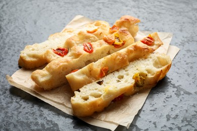Photo of Pieces of delicious focaccia with tomatoes on gray textured table, closeup