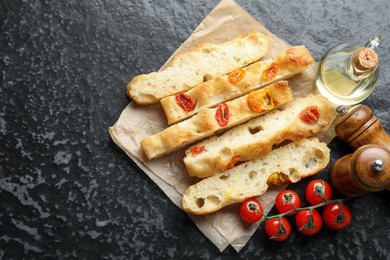 Photo of Pieces of delicious focaccia with tomatoes, spices and oil on dark textured table, flat lay. Space for text