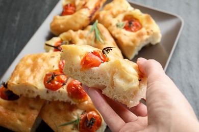 Photo of Woman holding piece of delicious focaccia with tomatoes and spices at table, closeup