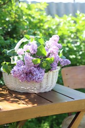 Photo of Beautiful lilac flowers in wicker basket on wooden table in garden