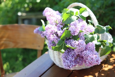 Photo of Beautiful lilac flowers in wicker basket on wooden table in garden, closeup. Space for text