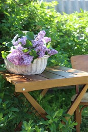 Photo of Beautiful lilac flowers in wicker basket on wooden table in garden