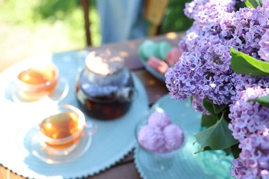 Photo of Beautiful lilac flowers, sweets and tea on table in garden, closeup