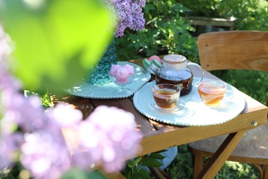 Photo of Beautiful lilac flowers, sweets and tea on wooden table in garden