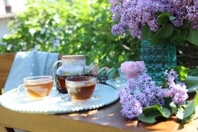 Photo of Beautiful lilac flowers, sweets and tea on wooden table in garden