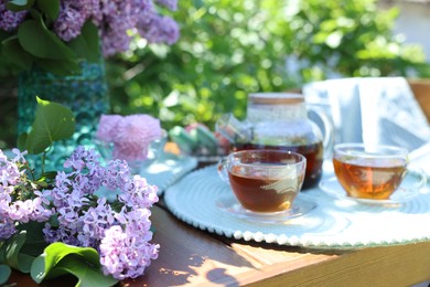 Photo of Beautiful lilac flowers, sweets and tea on wooden table in garden, closeup