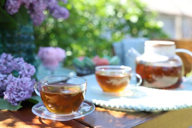 Photo of Beautiful lilac flowers and tea on wooden table in garden, closeup