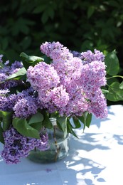 Photo of Beautiful lilac flowers in vase on table in garden, closeup