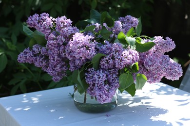 Photo of Beautiful lilac flowers in vase on table in garden
