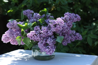 Photo of Beautiful lilac flowers in vase on table in garden